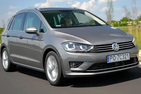 Szary Volkswagen Sportsvan jedzie po drodze. Kierowca w okularach prowadzi auto.