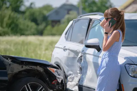 Kobieta rozmawia przez telefon obok dwóch uszkodzonych samochodów po kolizji.