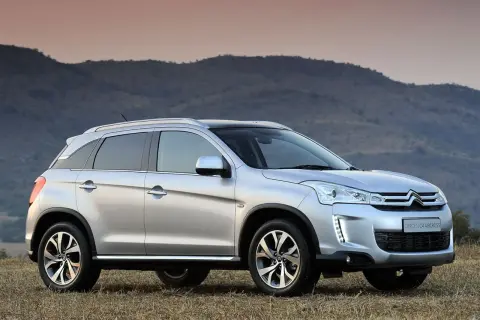 Srebrny Citroën C4 Aircross stoi na trawiastym wzgórzu, z górami w tle.
