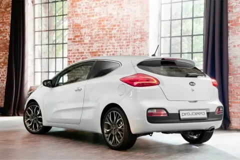 Biały Kia Pro_Ceed 1.6 benzyna z eleganckimi felgami stoi w stylowym wnętrzu z ceglaną ścianą i dużymi oknami.