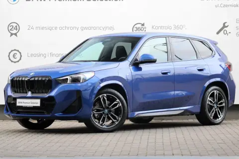 Niebieskie BMW iX1 na tle białej ściany z informacjami o gwarancji i finansowaniu. Sprawdź atrakcyjną bmw ix1 cena!