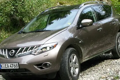 Brązowy Nissan Murano na kamienistej drodze, otoczony zielenią.