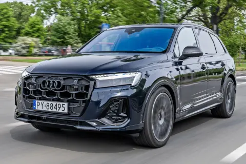 Elegancki, ciemny Audi Q7 2026 pędzi po drodze, otoczony zielenią.