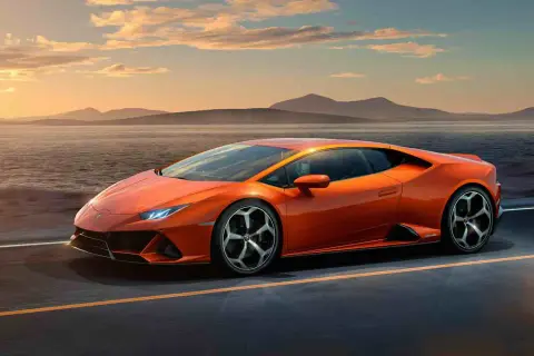 Pomarańczowy Lamborghini Huracan Evo pędzi wzdłuż malowniczego wybrzeża o zachodzie słońca.