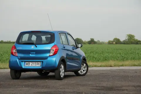 Niebieski Suzuki Celerio zaparkowany na drodze polnej, z polem kukurydzy w tle.