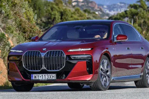 Czerwone BMW serii 7 z kierowcą za kierownicą, jadące po krętej drodze.