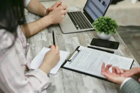 Osoby przy stole analizują dokument "Home Insurance Policy". Kobieta notuje, mężczyzna patrzy na laptopa. Może to być związane z wefox wypowiedzenie oc.