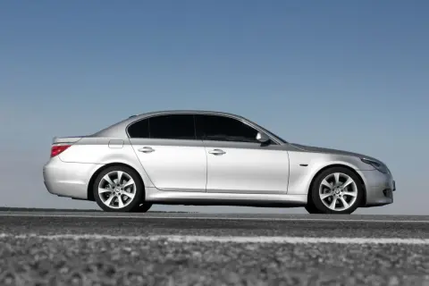 Srebrne BMW 5 E60 na tle błękitnego nieba, zaparkowane na drodze.