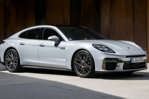 Biały Porsche Panamera Turbo S z czarnym dachem, zaparkowany przed rustykalną ścianą.