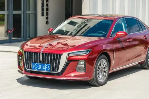 Elegancki, czerwony Hongqi H5 lśni w słońcu przed nowoczesnym budynkiem.