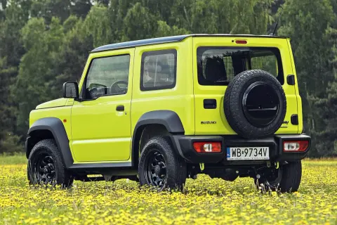 Jaskrawożółty Suzuki Jimny na tle łąki z żółtymi kwiatami. Sprawdź aktualną suzuki jimny cena i możliwości tego terenowego auta.