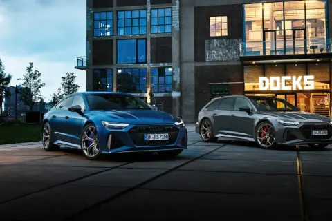 Dwa Audi RS6: niebieski sedan i szary Avant, zaparkowane przed budynkiem z napisem "DOCKS".