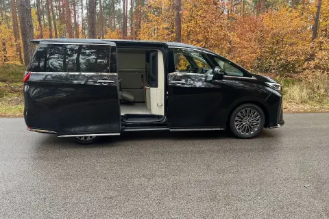 Lexus LM 350h w czarnym kolorze, z otwartymi drzwiami, prezentuje luksusowe wnętrze. Otoczony jesiennym lasem.