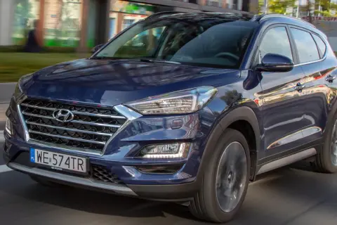 Ciemnoniebieski Hyundai Tucson 2025 w ruchu miejskim, z widocznym grillem i reflektorami.