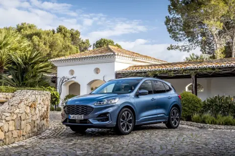 Niebieski Ford SUV Kuga, jeden z popularnych ford suv modele, zaparkowany na brukowanym podjeździe przed białym domem z czerwoną dachówką.