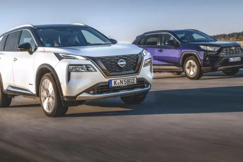 Biały Nissan X-Trail i fioletowy SUV jadą po drodze.