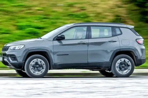 Szary Jeep Compass 4xe w ruchu, z rozmytym zielonym tłem.