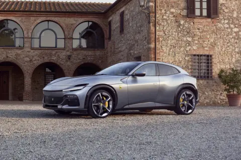 Srebrny Ferrari SUV Purosangue zaparkowany przed kamiennym budynkiem z łukowymi oknami.