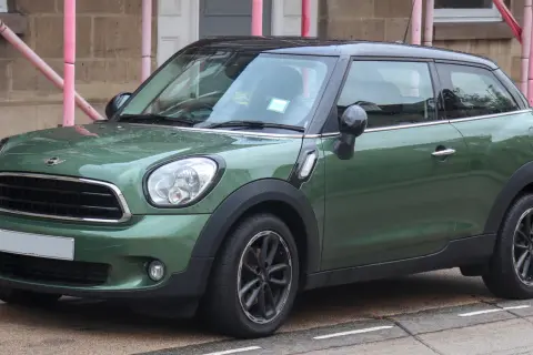 Zielony mini paceman z czarnym dachem stoi na ulicy, mokry od deszczu.
