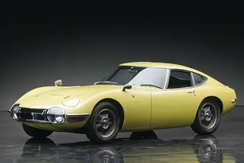 Żółta Toyota 2000GT z lat 60. prezentuje swoje klasyczne linie na błyszczącej podłodze.