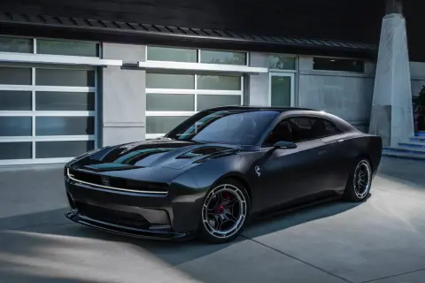Nowoczesny, ciemnoszary Dodge Daytona z charakterystycznym pasem LED z przodu, zaparkowany przed nowoczesnym budynkiem z garażem.