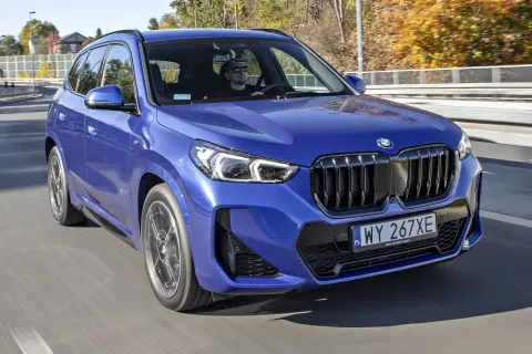 Niebieskie BMW X1 w ruchu drogowym. Kierowca w okularach przeciwsłonecznych. Sprawdź aktualną bmw x1 cena.