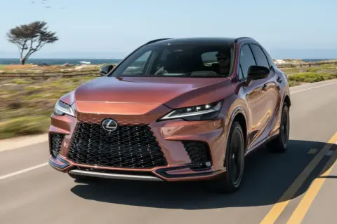 Miedziany Lexus RX 500h jedzie wzdłuż wybrzeża. Słońce odbija się od jego lśniącej karoserii.
