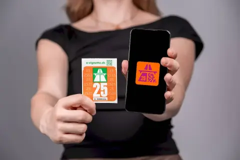 Kobieta trzyma winietę szwajcarską i smartfon z aplikacją e-winiety.