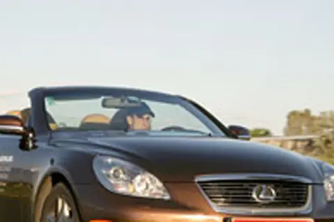 Brązowy kabriolet Lexus SC430 z otwartym dachem, kierowca w czapce, jazda w słoneczny dzień.