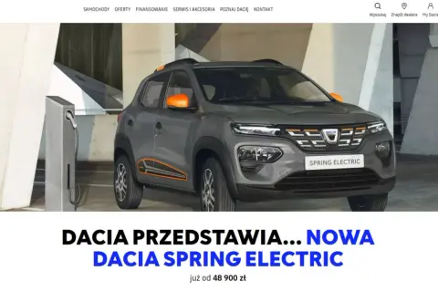 Szara dacia elektryczna Spring Electric z pomarańczowymi akcentami ładuje się przy stacji.