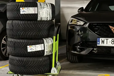 Cztery nowe opony Michelin CrossClimate 2 na wózku, gotowe do montażu w czarnym aucie. To najlepsze opony wielosezonowe dla pewności jazdy przez cały rok.