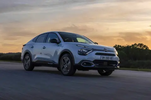 Jasnoszary Citroën C4X sunie po drodze podczas zachodu słońca.
