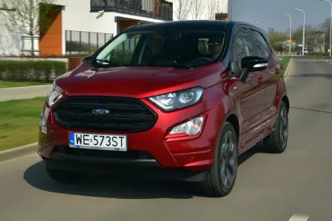 Czerwony Ford Ecosport w ruchu miejskim. Kierowca w okularach przeciwsłonecznych. Wiele pozytywnych ford ecosport opinie potwierdza jego miejski charakter.
