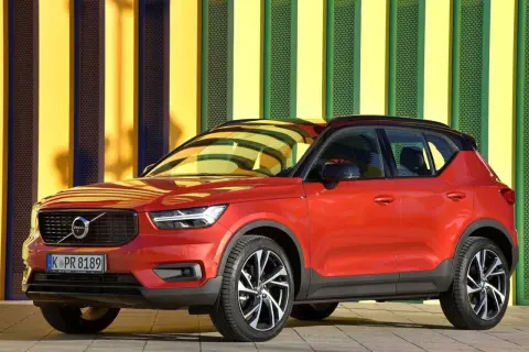 Czerwone Volvo XC40 na tle kolorowej ściany. Wiele osób szuka volvo xc40 opinie przed zakupem.