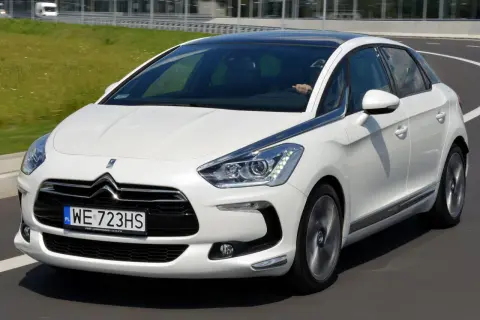 Biały Citroen DS5 na drodze. Kierowca trzyma kierownicę. Wiele osób chwali ten model, a jego opinie są pozytywne.