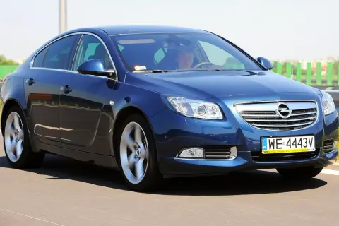 Niebieski Opel Insignia 2.0 Turbo pędzi po drodze, kierowca skupiony na trasie.
