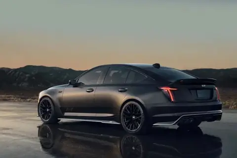 Mroczny Cadillac CT5 z czarnymi felgami i spojlerem na tle górskiego krajobrazu o zachodzie słońca.