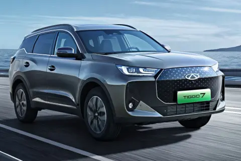 Szary SUV Chery Tiggo 7 z zielonym napisem TIGGO 7 na grillu, jadący po drodze.