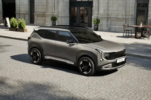 Nowy model Kia, szary SUV, parkuje na brukowanej ulicy przed eleganckim budynkiem.