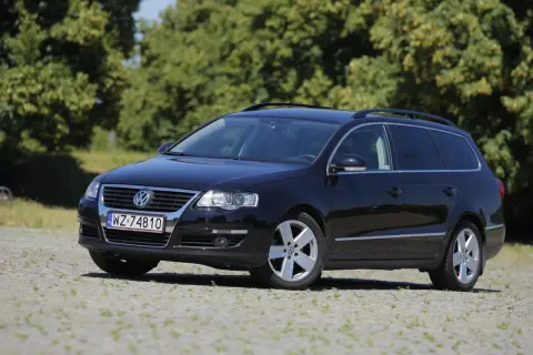 Czarny Volkswagen Passat kombi, model r36, zaparkowany na kamienistym podjeździe, z zielonymi drzewami w tle.