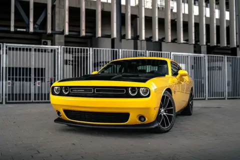 Żółty Dodge Challenger 5.7 Hemi z czarną maską, zaparkowany przed nowoczesnym budynkiem.