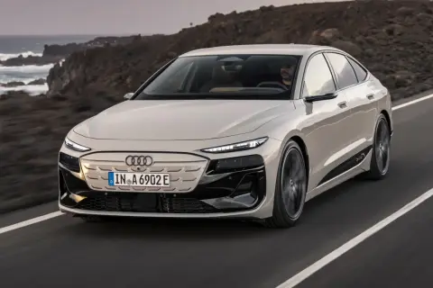 Elegancki Audi A6 e-tron w kolorze jasnego beżu przemierza malowniczą, skalistą trasę nad oceanem.