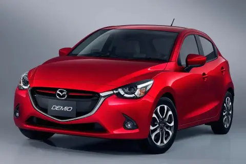 Czerwona Mazda Demio z błyszczącym lakierem i charakterystycznym grillem.