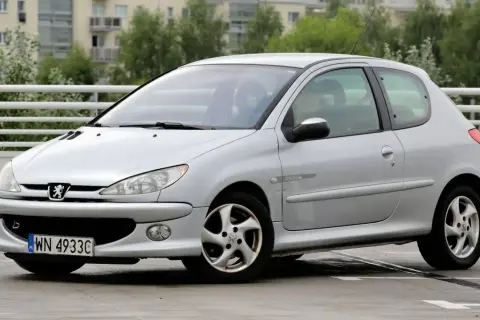 Srebrny Peugeot 206 1.4 benzyna na parkingu. Auto ma sportowy wygląd i jest w dobrym stanie.
