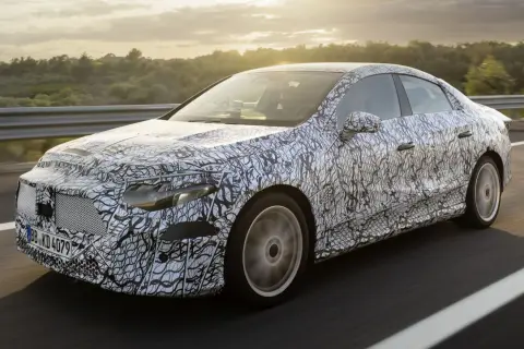 Zamaskowany prototypowy Mercedes CLA 2025 na drodze, z widokiem na zachodzące słońce i drzewa w tle.
