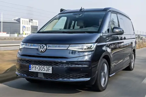 Ciemny Volkswagen California w ruchu drogowym. Sprawdź aktualną volkswagen california cena i planuj podróże!