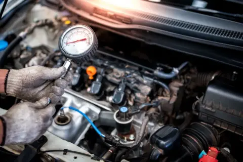 Mechanik sprawdza ciśnienie w cylindrach silnika benzynowego za pomocą manometru.