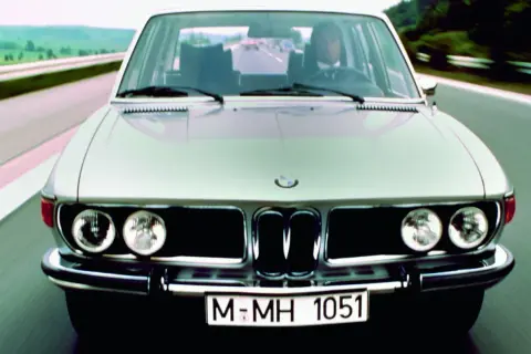 Klasyczne bmw e3 pędzi autostradą. Kierowca w garniturze pewnie prowadzi lśniący samochód.