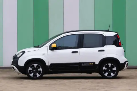 Biały fiat pandina z żółtymi lusterkami stoi na tle zielono-białej ściany.