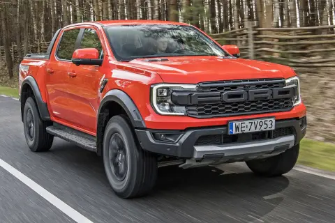 Pomarańczowy Ford Raptor jedzie po drodze w lesie. Sprawdź aktualną ford raptor cena i możliwości tego potężnego pickupa.